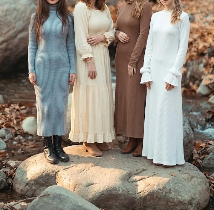 Four women modeling cozy modest pre-fall wardrobe maxi dresses in long-sleeve knit styles, including light blue ribbed turtleneck, cream tiered, chocolate brown, and white bell-sleeve dresses outdoors.