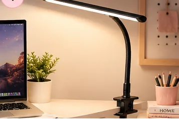 Black clamp-on LED desk lamp illuminating a home office workspace